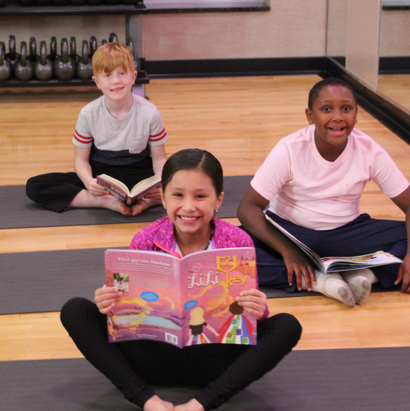 Children smiling at the camera in Open Book, a LiYo Literacy Yoga Fusion pose